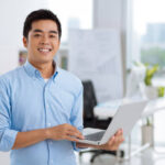 Boldog fiatal ázsiai szoftverfejlesztő laptoppal a kezében